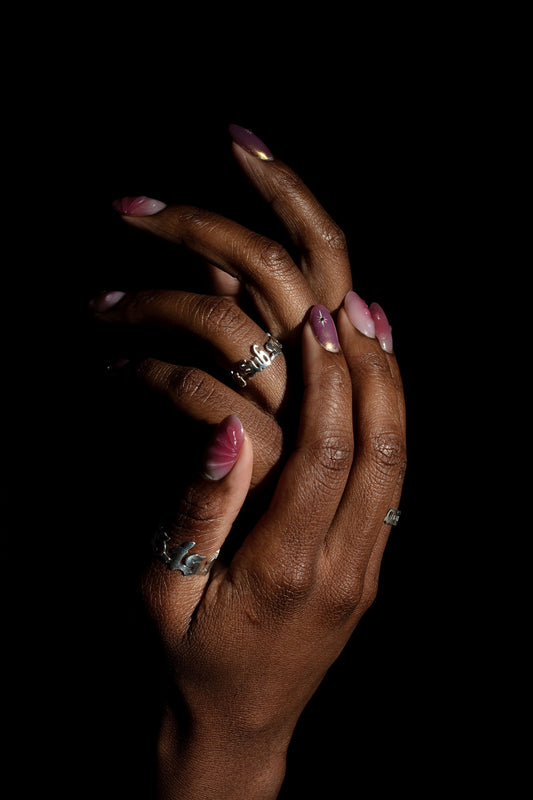 Close-up of two hands adorned with Sterling 925 silver rings engraved with 'sub specie aeternitatis' and 'less is more.' The rings are worn on fingers with stylish nails in shades of pink and purple, with intricate designs highlighted against a dark background.