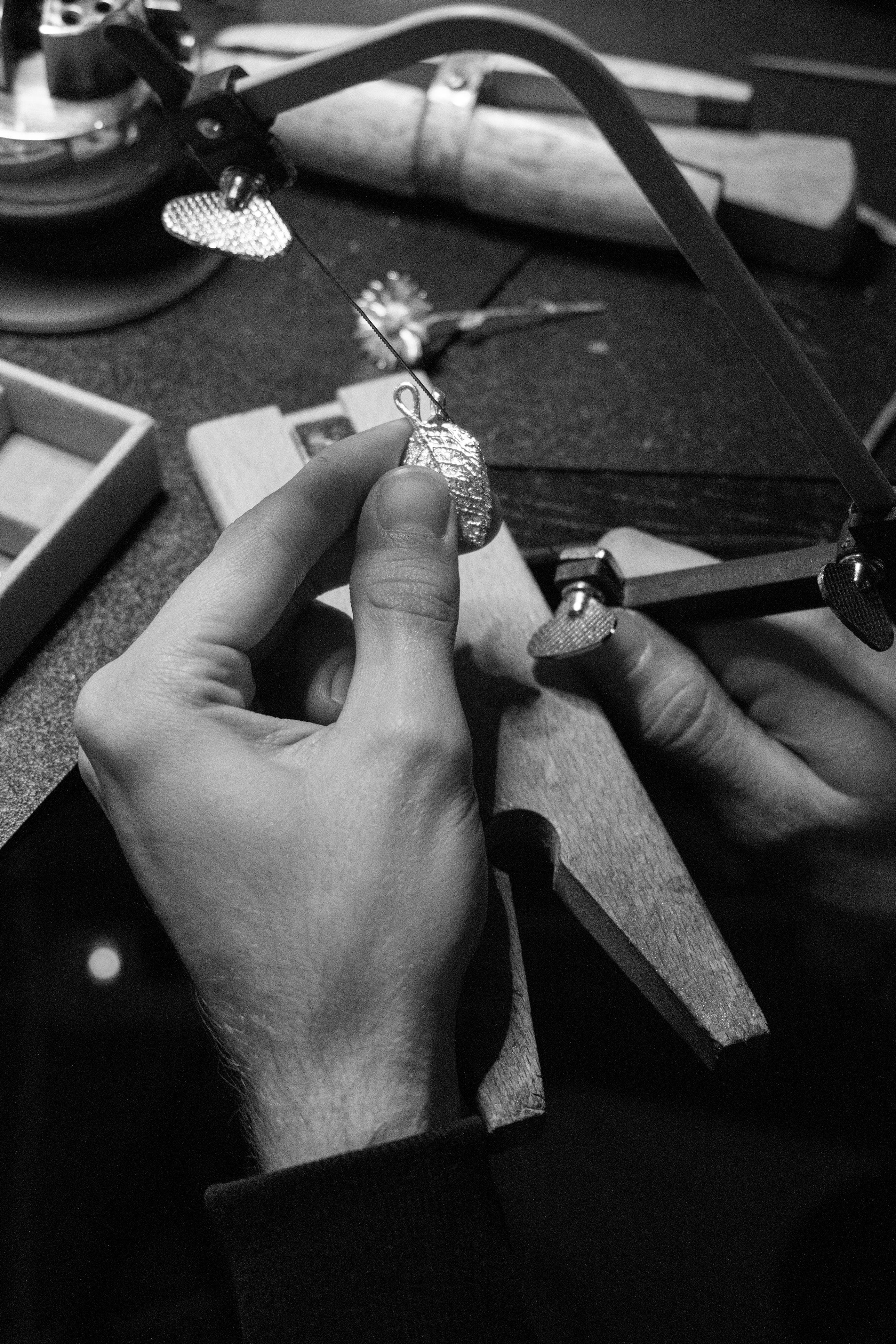 Close-up of hands working on jewelry with tools and materials on a table.