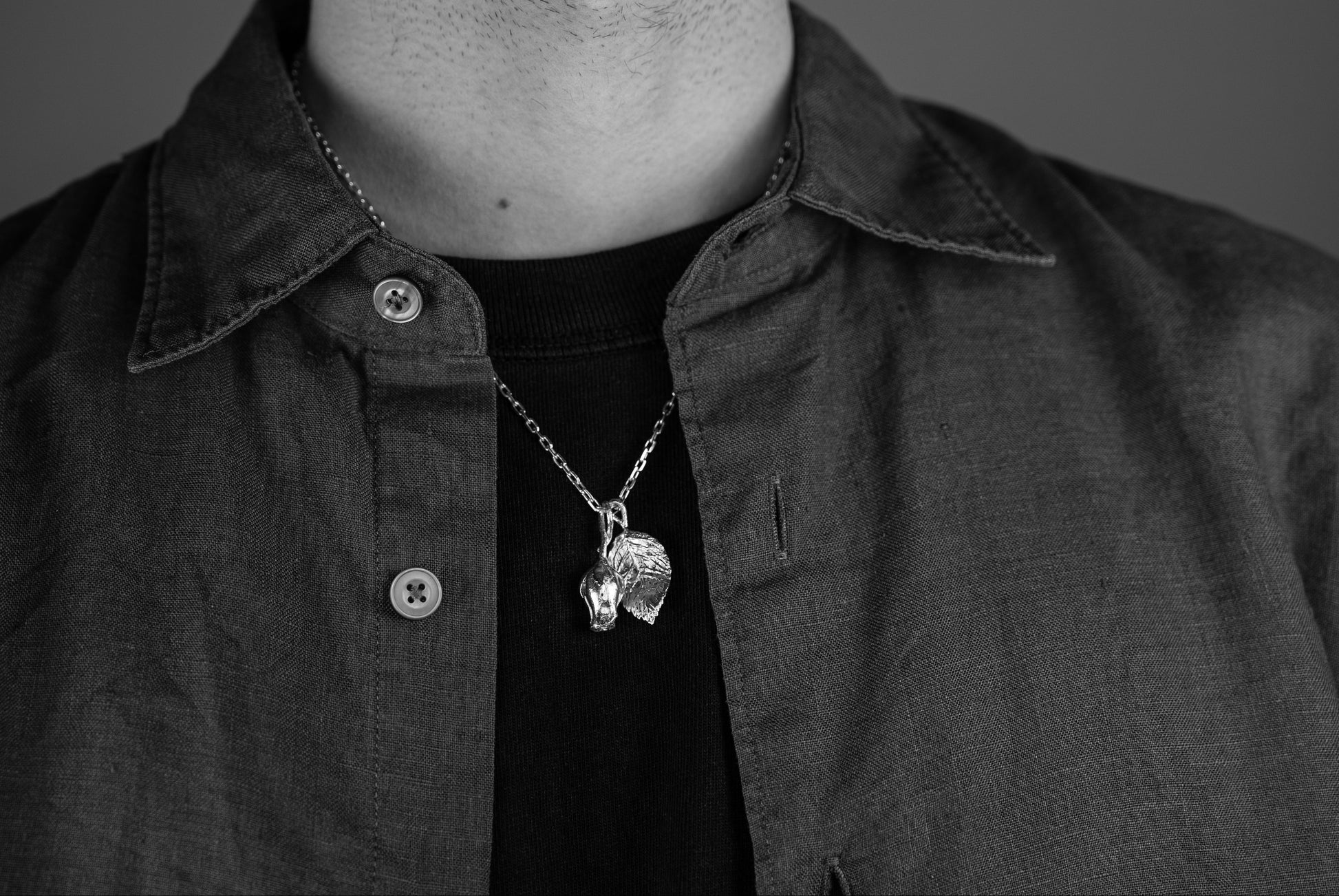 Person wearing a dark shirt with a necklace featuring a rode bud and leaf pendant against a neutral background