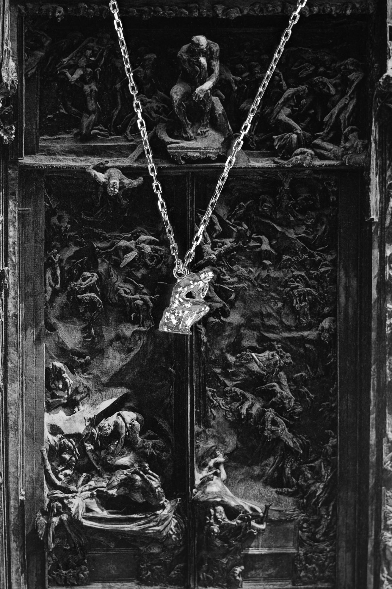 925 Sterling Silver pendant of 'The Thinker' statue by Rodin hanging from a chain, set against a dramatic black-and-white background of 'The Gates of Hell' sculpture by Rodin.