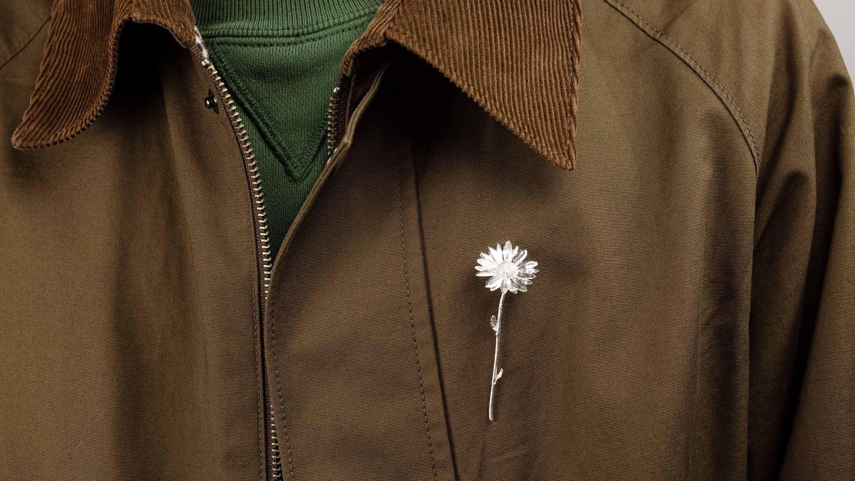 Close-up of a Sterling 925 silver daisy brooch pinned on a brown corduroy jacket. The brooch, featuring an intricate floral daisy design, stands out against the neutral tones of the jacket and green sweatshirt, emphasizing its delicate craftsmanship.