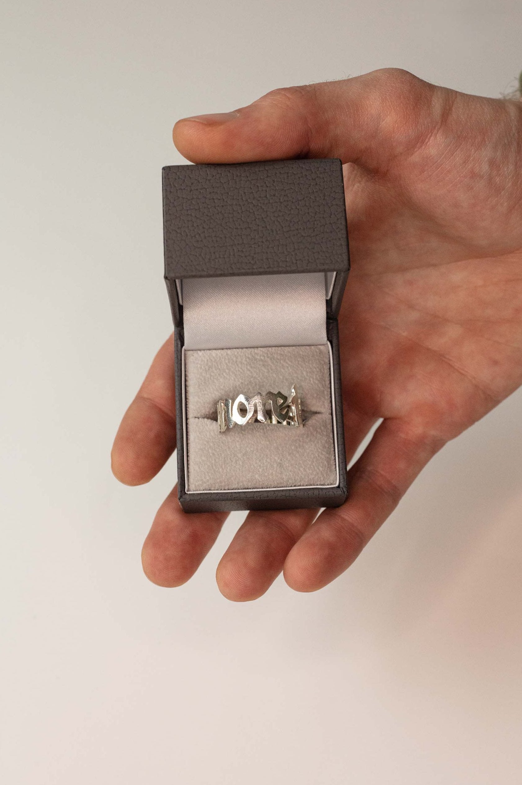 Sterling 925 silver ring engraved with 'more is more,' displayed in an open jewelry box held in a hand.