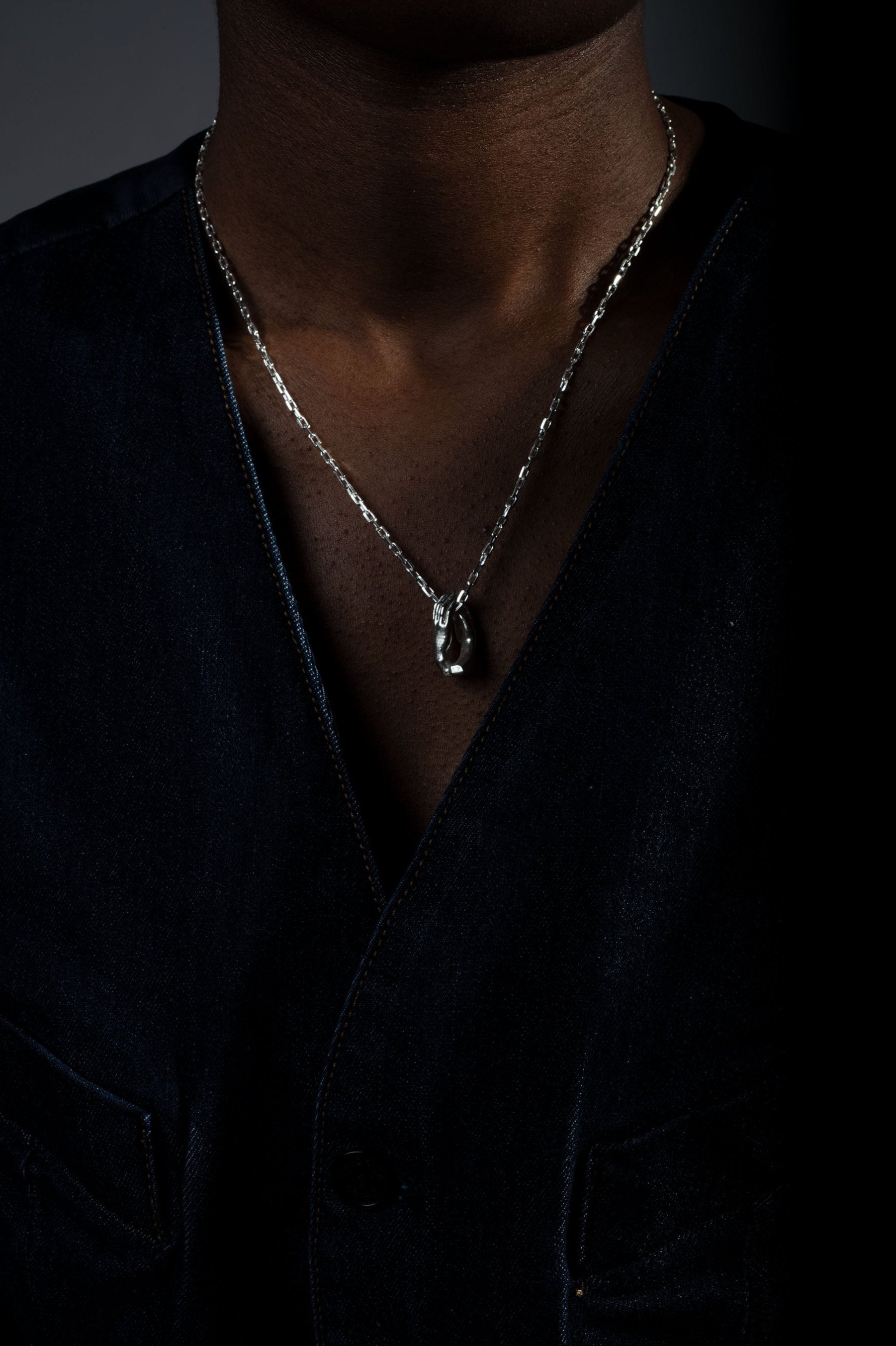 Sterling 925 silver pendant of Rodin's sculpture 'The Cathedral,' hanging from a chain around the neck of a person wearing a dark blue, buttoned vest.