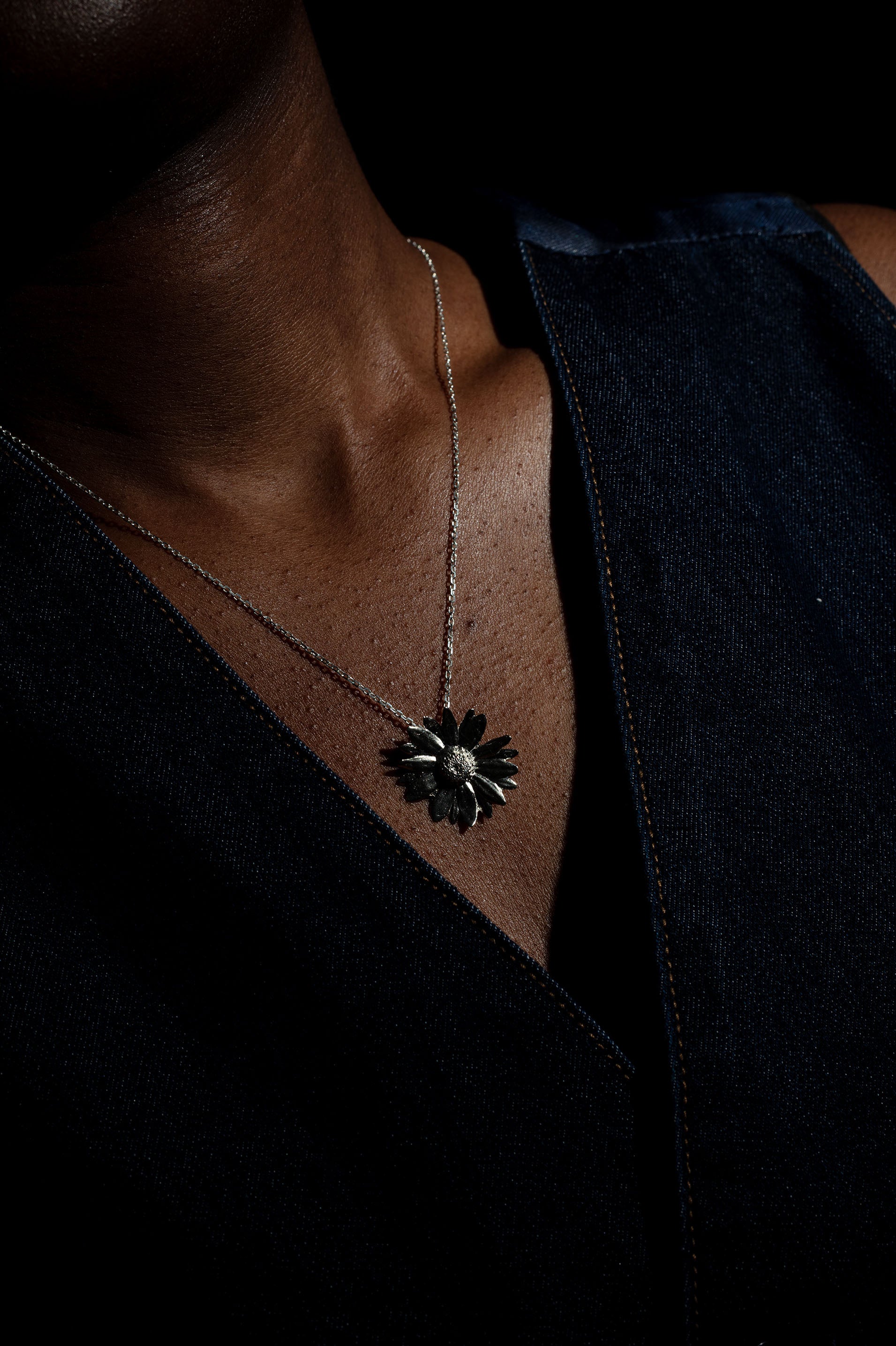 Sterling 925 silver daisy pendant hanging from a chain, worn on the neck of a person dressed in a dark denim top.