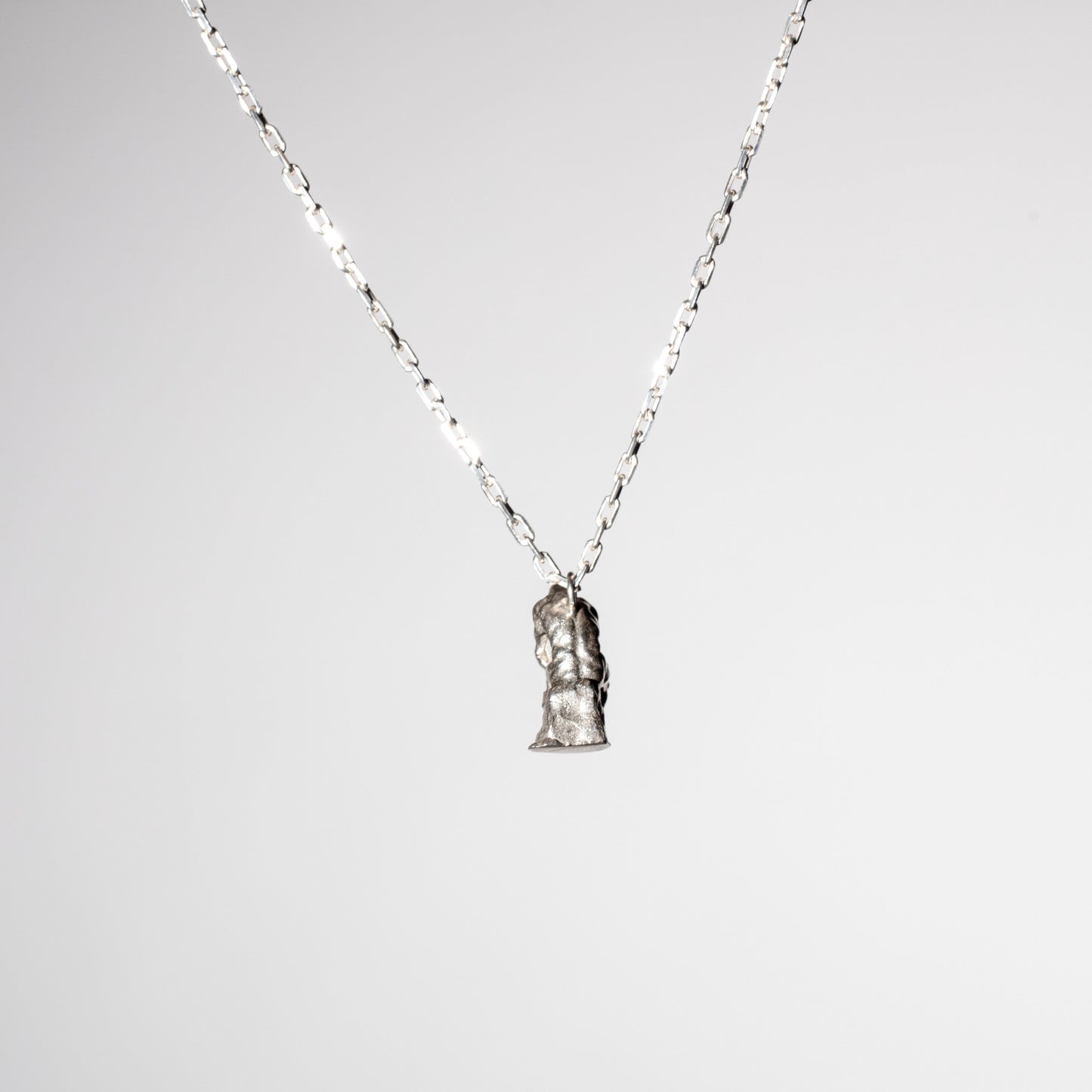 Product photo of a Sterling 925 silver pendant modeled after Rodin's sculpture 'The Thinker,' hanging from a silver chain, viewed from the back. The pendant features a small, detailed rendition of the seated figure in a contemplative pose, captured against a minimalist white background, emphasizing the craftsmanship and artistic design.