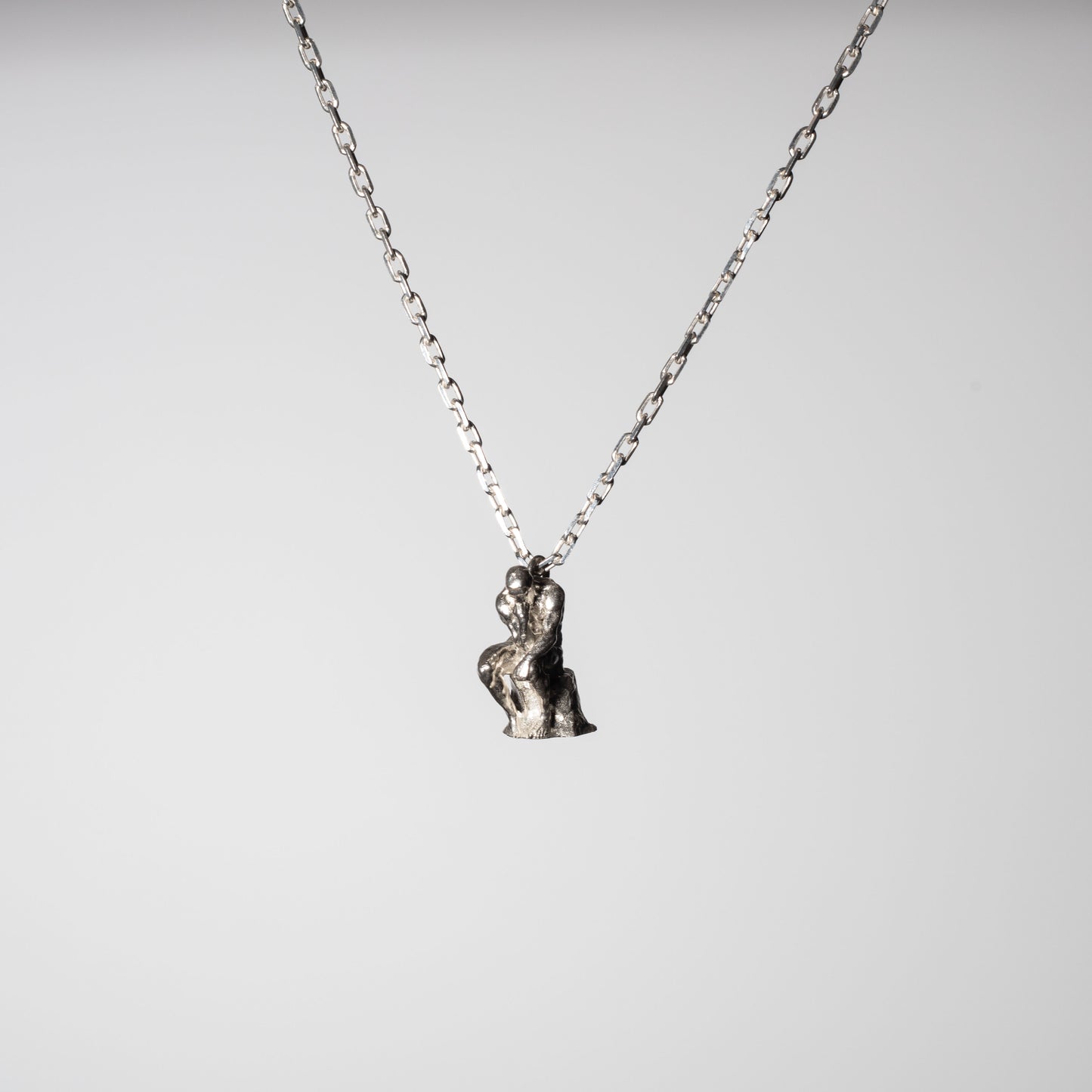 Product picture of a Sterling 925 silver pendant modeled after Rodin's sculpture 'The Thinker,' hanging from a silver chain. The pendant features a small, detailed rendition of the seated figure in a contemplative pose, captured against a minimalist white background, highlighting the craftsmanship and artistic design.