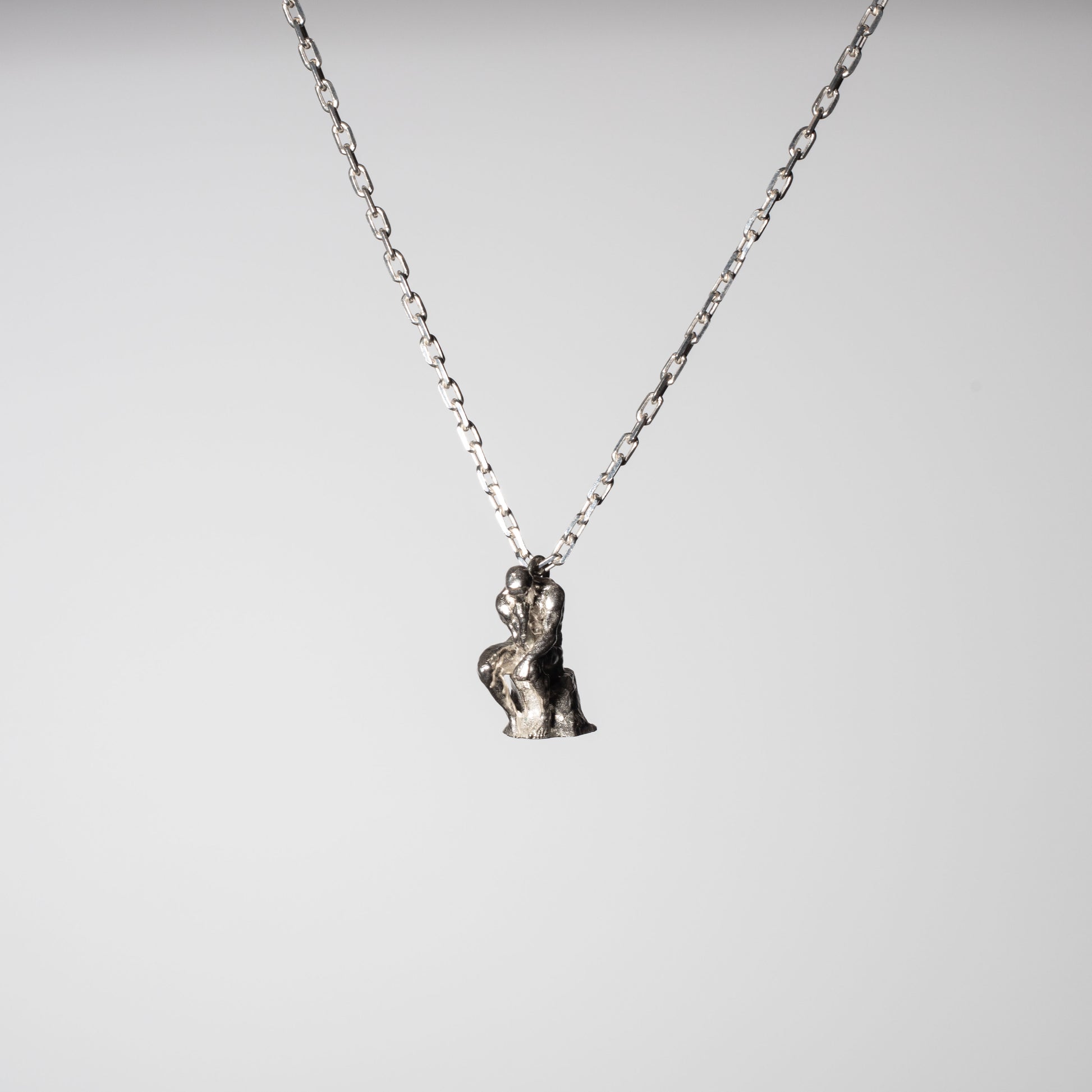 Product picture of a Sterling 925 silver pendant modeled after Rodin's sculpture 'The Thinker,' hanging from a silver chain. The pendant features a small, detailed rendition of the seated figure in a contemplative pose, captured against a minimalist white background, highlighting the craftsmanship and artistic design.